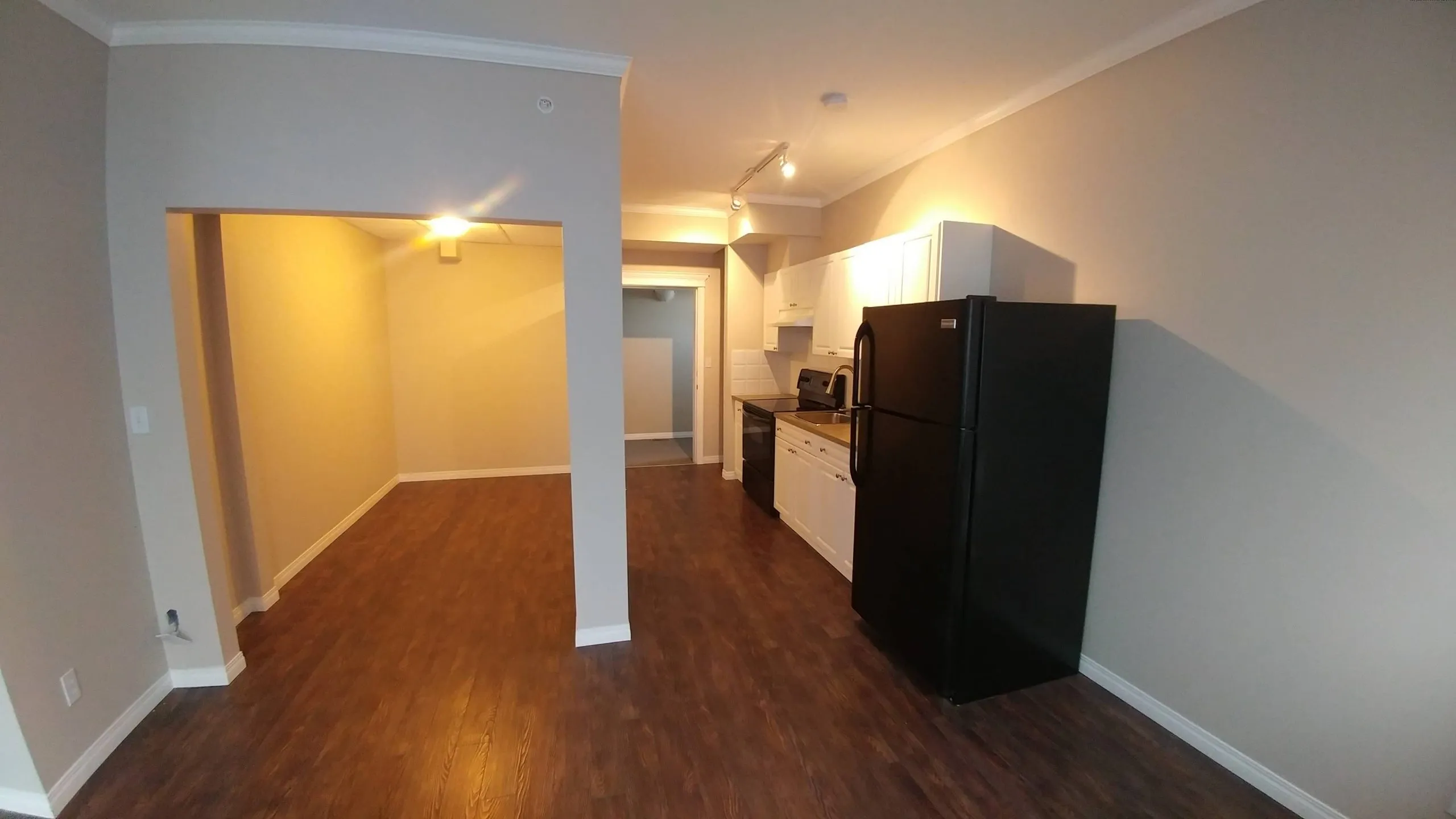 Empty studio suite with wood-look flooring and a kitchen along one wall