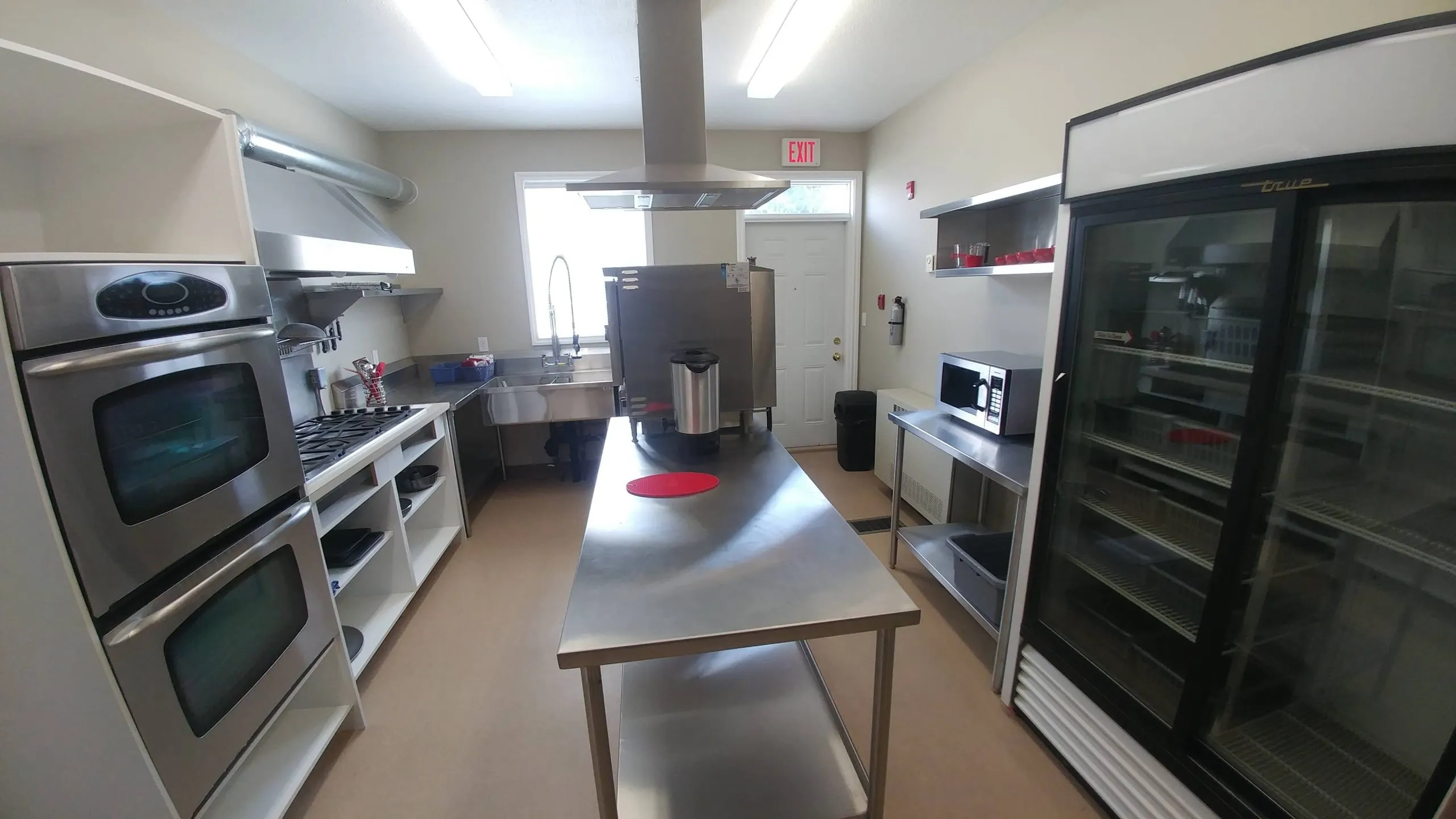 Commercial kitchen with double ovens, a range hood and a steel prep table