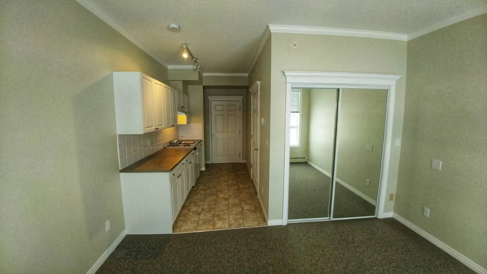 An empty studio suite with a galley kitchen and mirrored closet